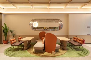 Ein modernes Interieur mit einer Sitzecke, ausgestattet mit runden Tischen und gepolsterten Stühlen, einer Wand mit dekorativem Spiegel und Topfpflanzen.