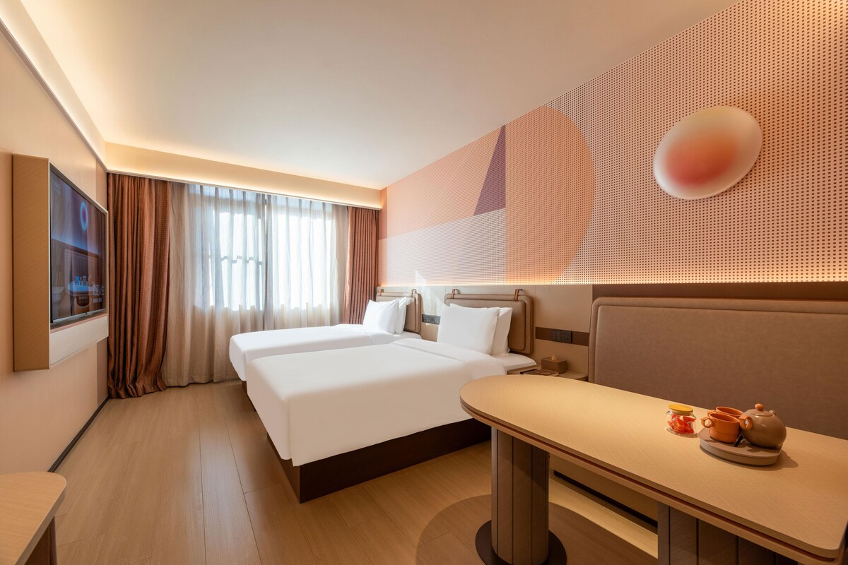 Ein Hotelzimmer mit zwei Betten, einem Schreibtisch, einem Fernseher und einer dekorativen Wandverkleidung.