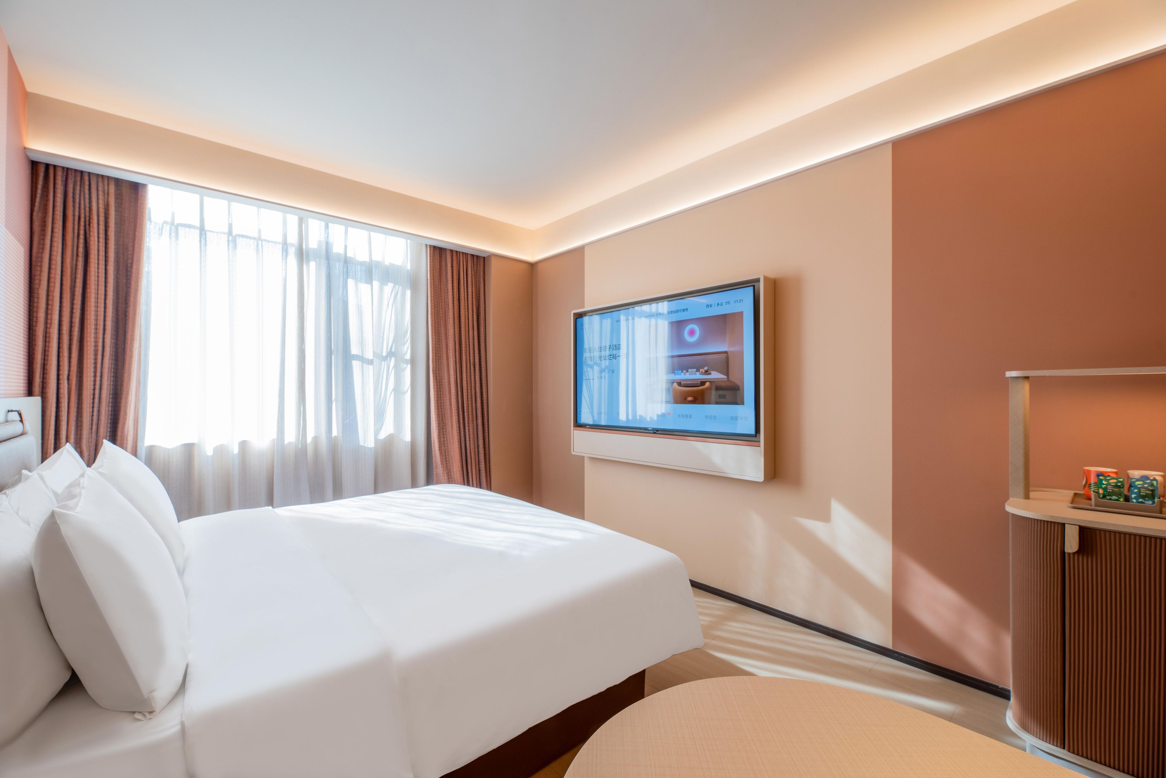 A hotel room with a bed, a television mounted on the wall, and a small table with items on it.