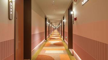 A hotel hallway with a carpeted floor, doors on both sides, and overhead lighting.