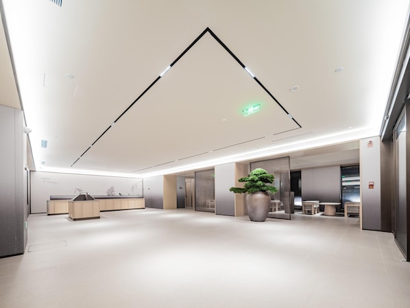 A spacious lobby with a modern design, featuring a large reception desk, a potted plant, and a clean, minimalist aesthetic.