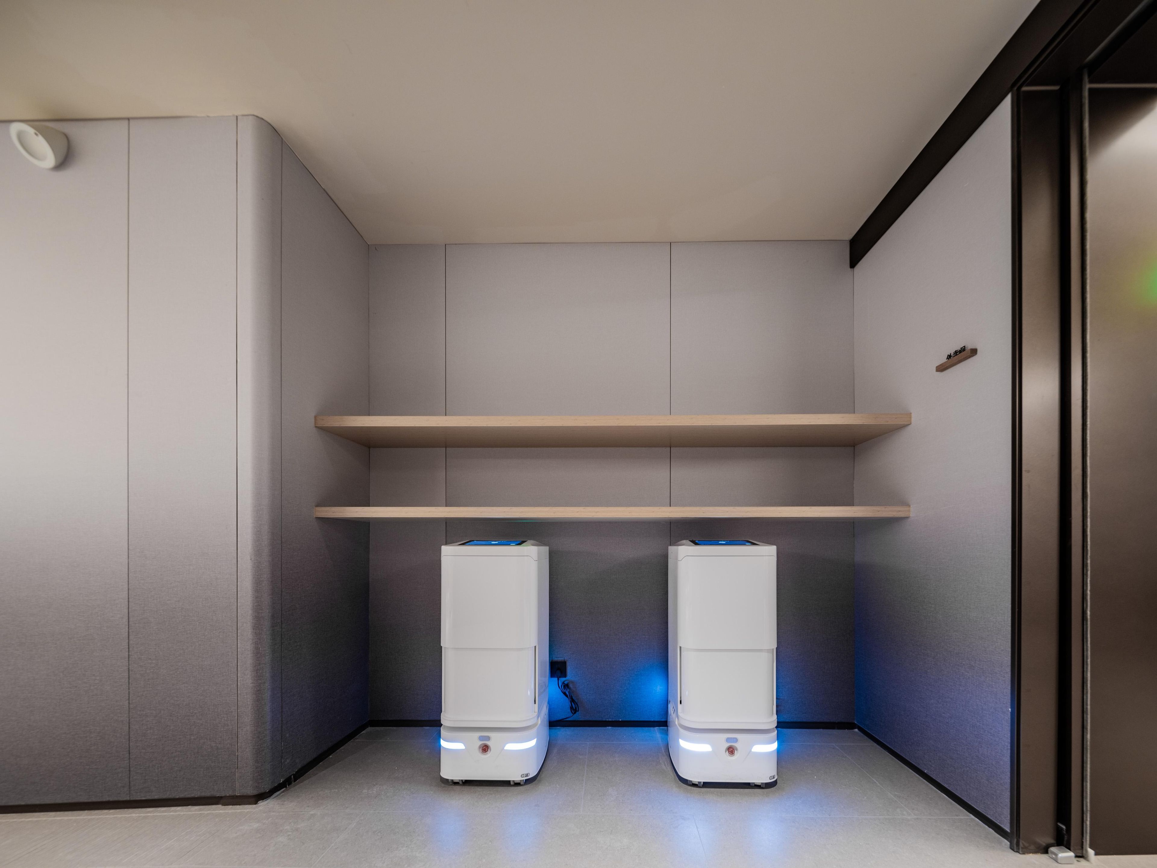 A modern room with two white devices on the floor, a wooden shelf above, and a small wooden plaque on the wall.