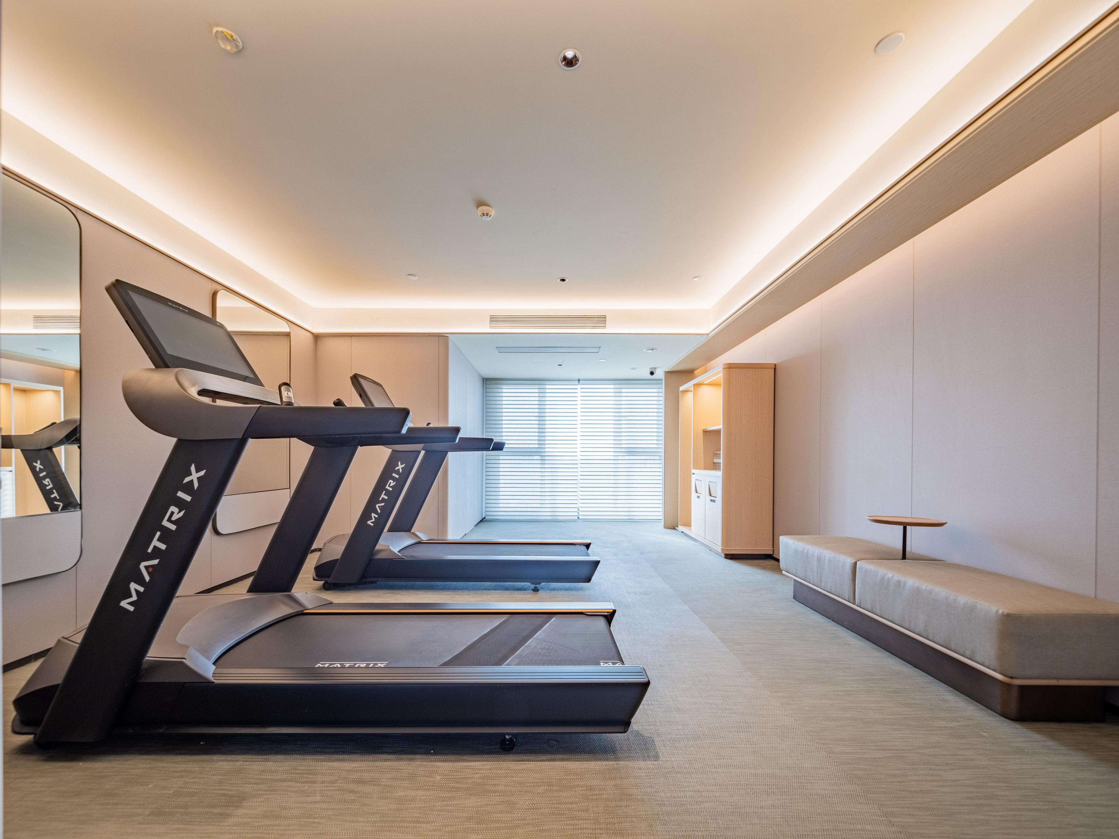 A modern hotel gym with treadmills, a seating area, and a view of the outside.
