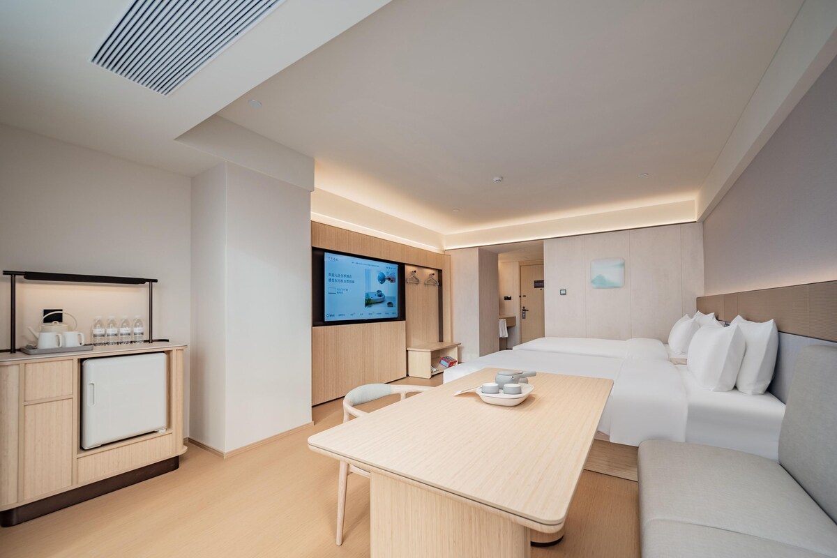 A modern hotel room with a bed, a desk, a TV, and a kitchenette.
