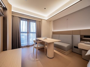 A modern hotel room with a dining table, a sofa, and a large window with curtains.