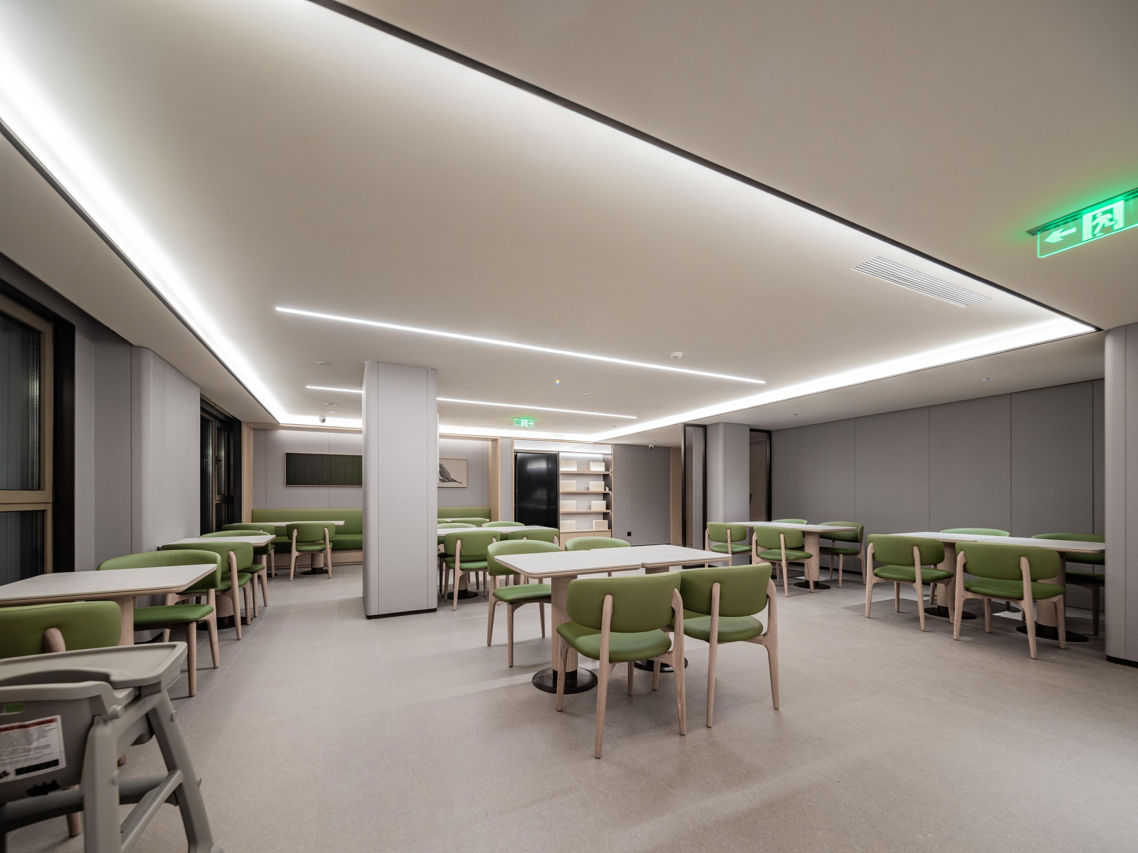 A modern dining area with tables and chairs, a bookshelf, and a green exit sign.