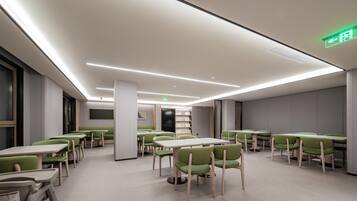 A modern dining area with tables and chairs, a bookshelf, and a green exit sign.