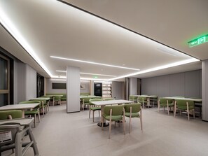 A modern dining area with tables and chairs, a bookshelf, and a green exit sign. - JI Hotel (xian Jiaotong University Qinglong Templ (Xi'an)
