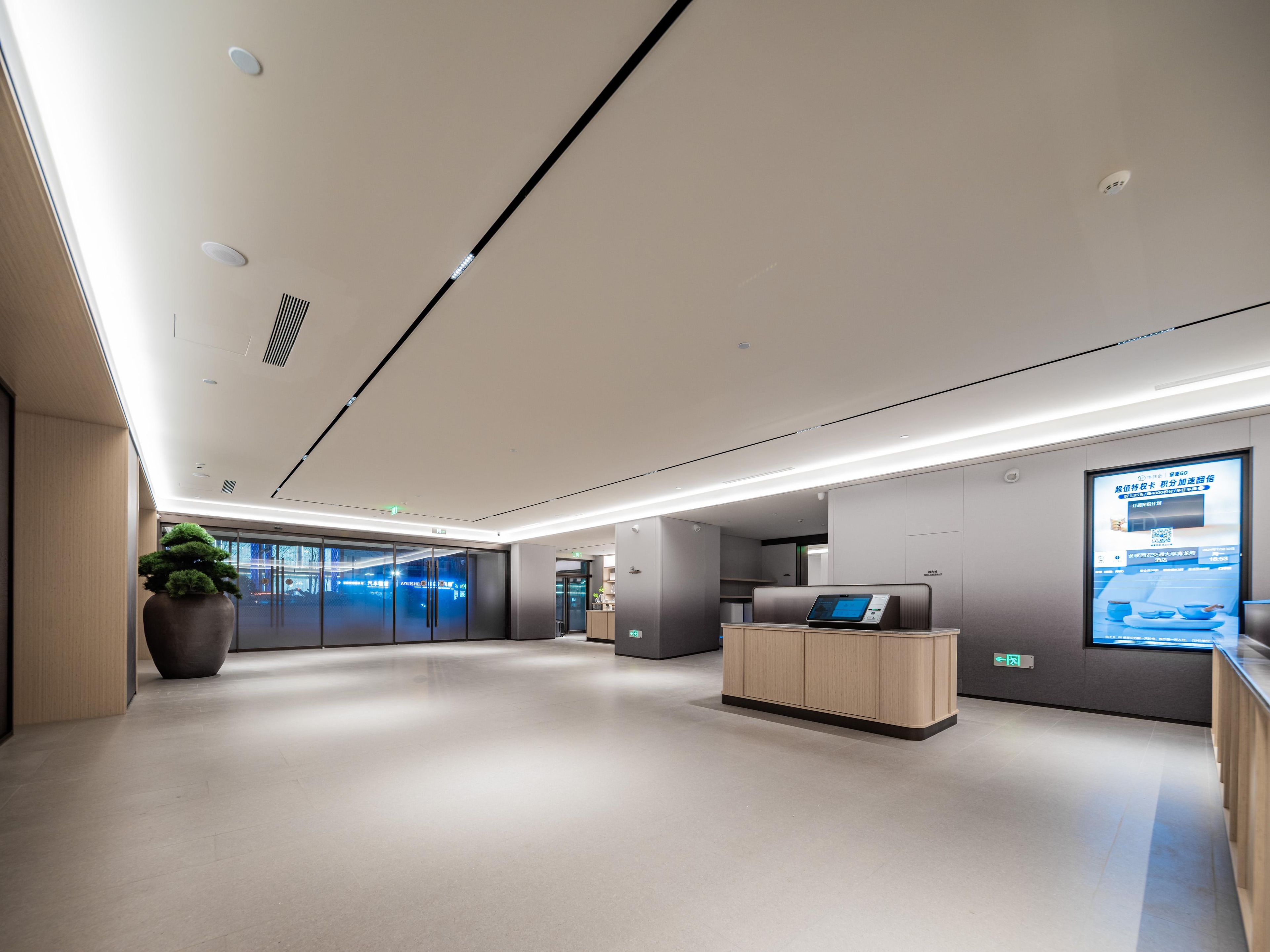 A modern lobby with a reception desk, a large potted plant, and a digital information screen.