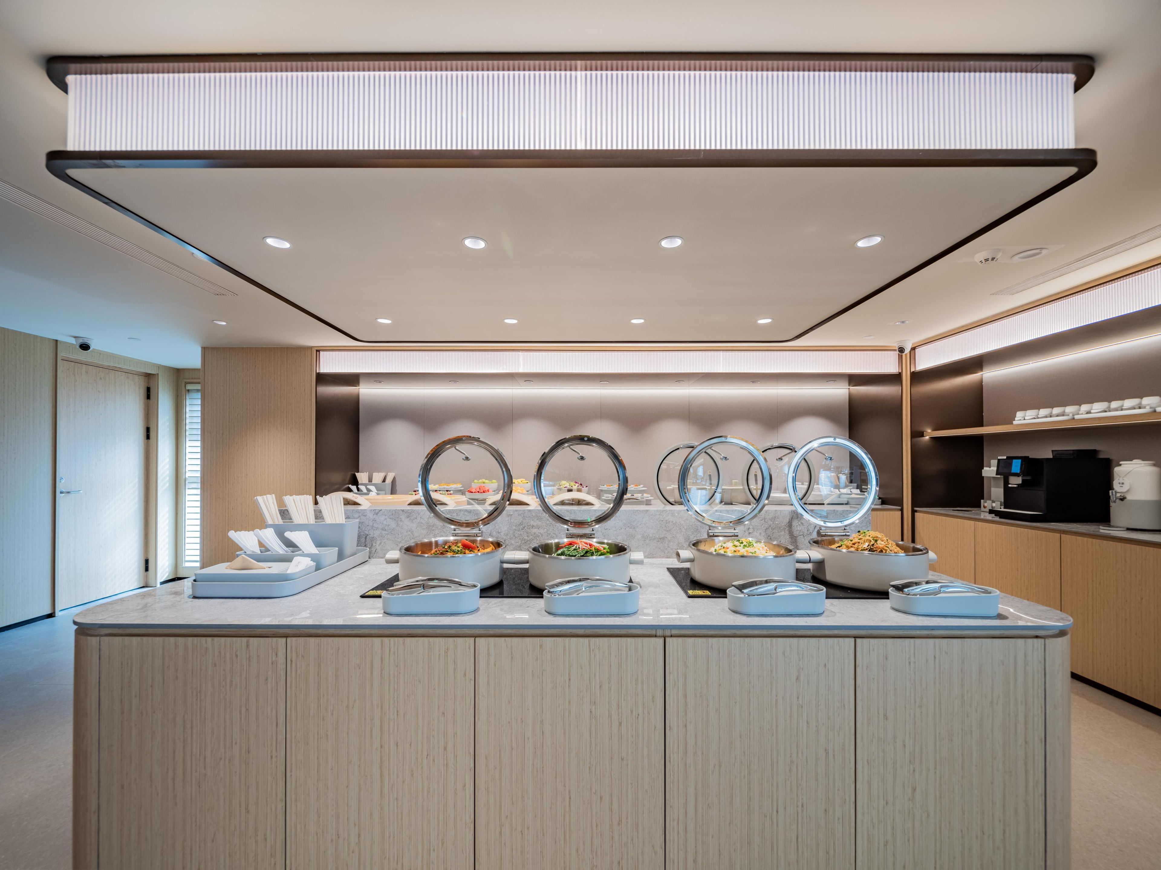 Un moderno montaje tipo buffet con varias estaciones de comida, una máquina de café y un diseño limpio y minimalista.