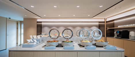 A modern buffet setup with multiple food stations, a coffee machine, and a clean, minimalist design.