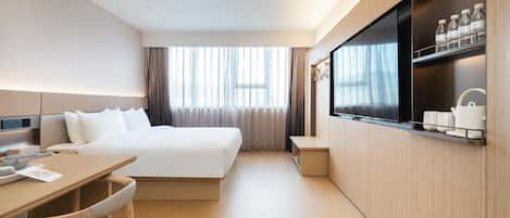 A modern hotel room with a bed, a desk, a chair, a TV, and a minibar.