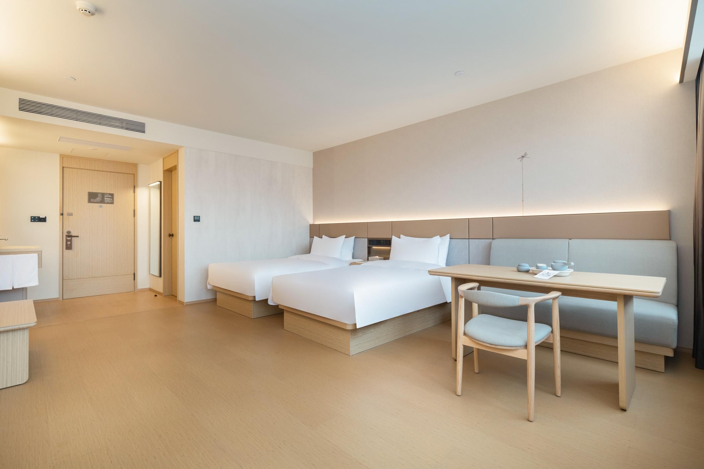 Ein Hotelzimmer mit zwei Betten, einem Schreibtisch, einem Stuhl und einem kleinen Tisch mit Tasse und Untertasse.