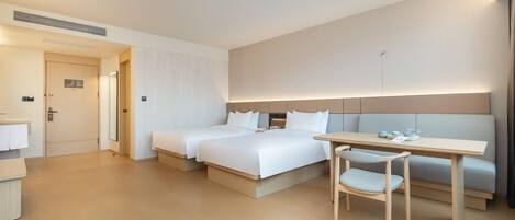 A hotel room with two beds, a desk, a chair, and a small table with a cup and saucer.
