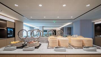 A buffet area with multiple food stations, including a bowl of fruit, a pot of soup, and several containers of rice.