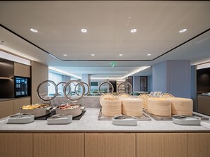 A buffet area with multiple food stations, including a bowl of fruit, a pot of soup, and several containers of rice.