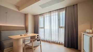 Une chambre d’hôtel moderne avec un bureau en bois, un banc rembourré, une chaise et un meuble de rangement.