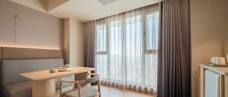 A modern hotel room with a wooden desk, a cushioned bench, a chair, and a cabinet.