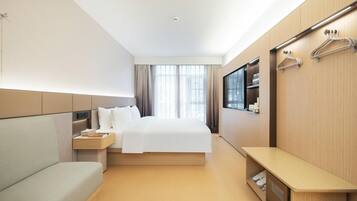 A modern hotel room with a bed, a sofa, a bedside table, a TV, and a wardrobe with a mirror.