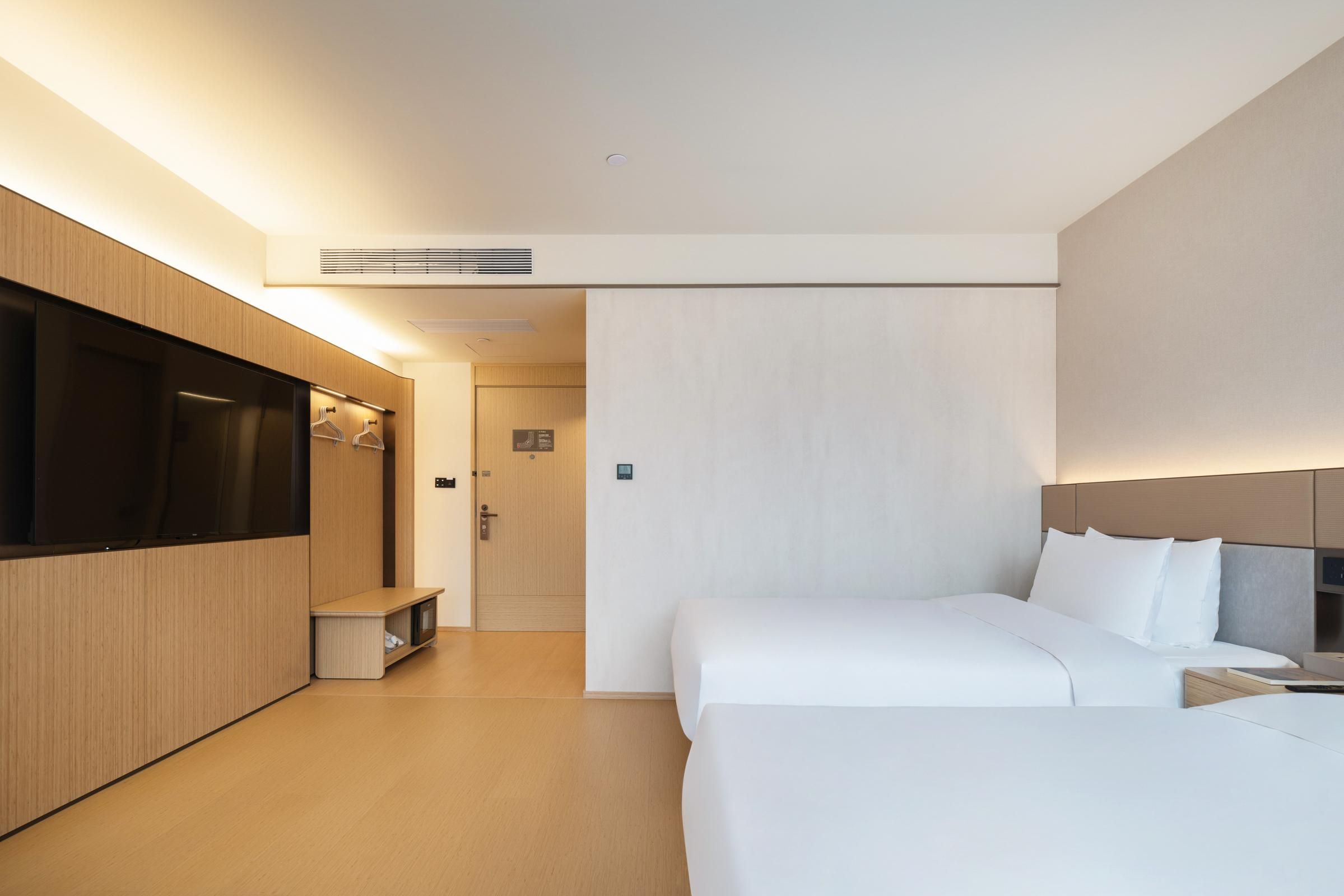 A modern hotel room with a bed, bedside table, and a flat-screen TV mounted on the wall.