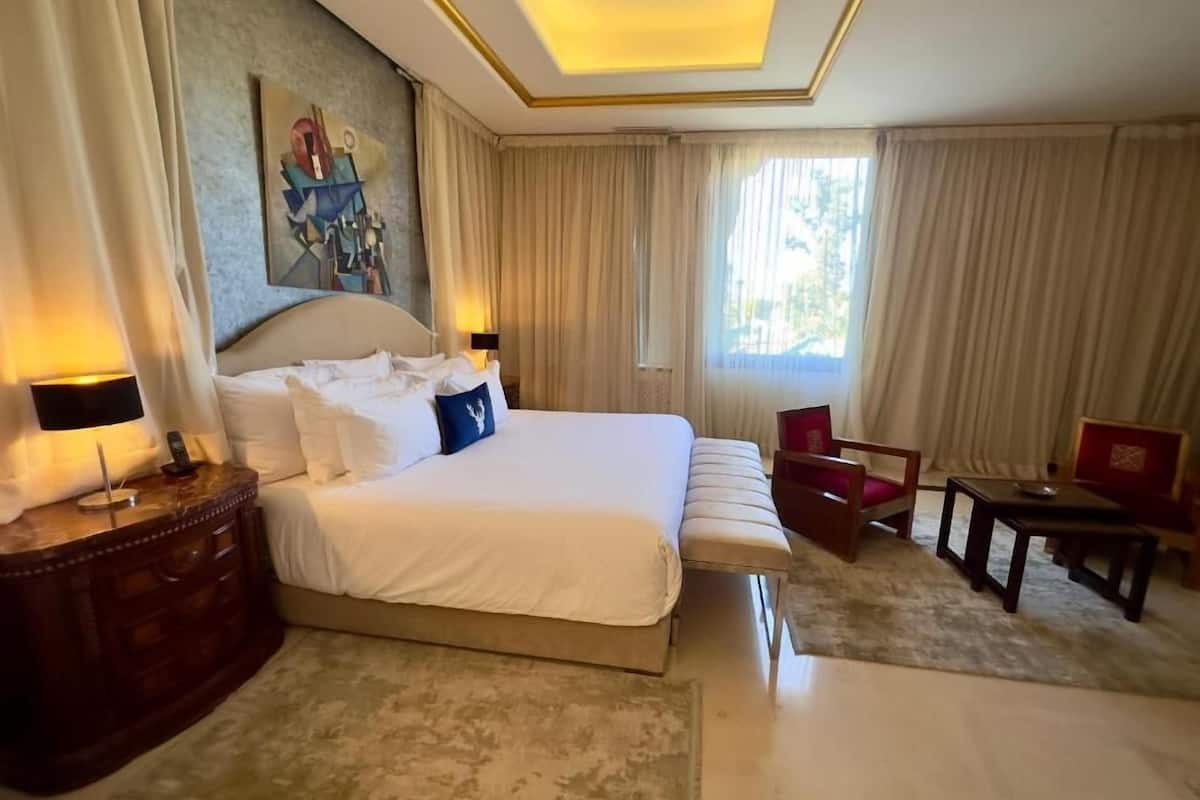 A hotel room with a large bed, a desk, a chair, and a painting on the wall.