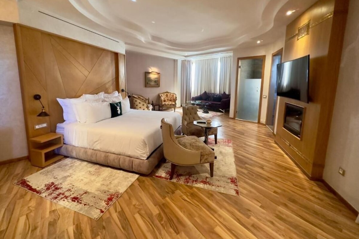 A hotel room with a large bed, a TV, a seating area with a chair and a small table, and a wooden floor.