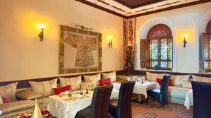 A dining area with a map artwork, cushioned seating, tables with white tablecloths, and decorative wall sconces. - Sillage Palace (Marrakech)