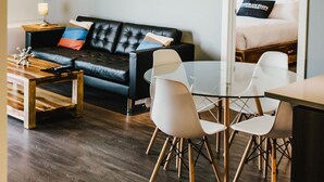 A modern living room with a black leather sofa, a glass coffee table, and white chairs. - The Spot (Winnipeg)