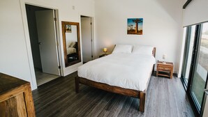 A bedroom with a wooden bed, a nightstand, a mirror, and a window with a view. - The Spot (Winnipeg)