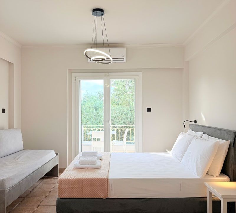 A hotel room with a bed, a sofa, a balcony, and an air conditioning unit.