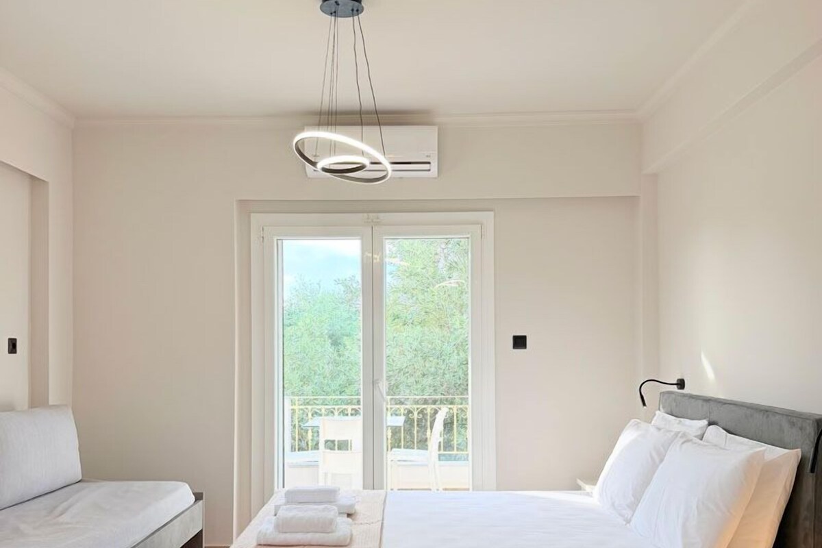 A hotel room with a bed, a sofa, a balcony, and an air conditioning unit.