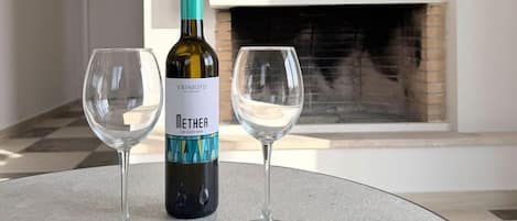 A bottle of wine and two glasses on a round table with a fireplace in the background.