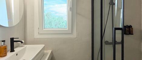 A bathroom with a white sink, a mirror, a window, and a glass-enclosed shower.