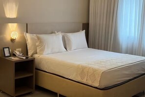 Ein Hotelzimmer mit einem Bett, einem Nachttisch mit Telefon und Lampe sowie einem Fenster mit Vorhängen.