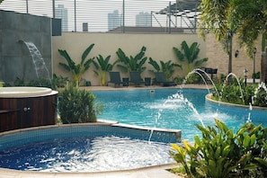 Una piscina con idromassaggio, lettini e piante tropicali.