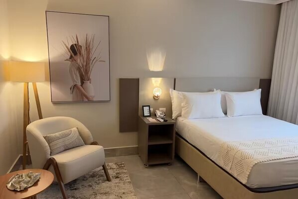 Ein Hotelzimmer mit einem Bett, einem Sessel, einem Nachttisch mit Lampe und einem gerahmten Bild an der Wand.