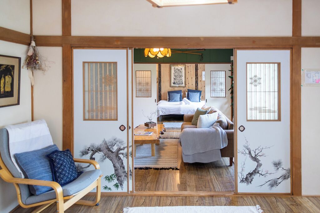 Una habitación japonesa tradicional con suelo de tatami, una cama de madera baja y una puerta corredera que da a un dormitorio.