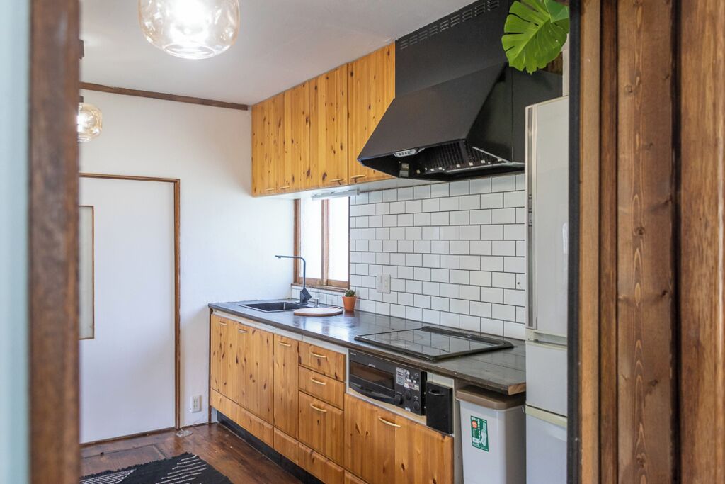 Una cocina con gabinetes de madera, una campana extractora negra, un protector contra salpicaduras blanco de azulejos y un lavavajillas.