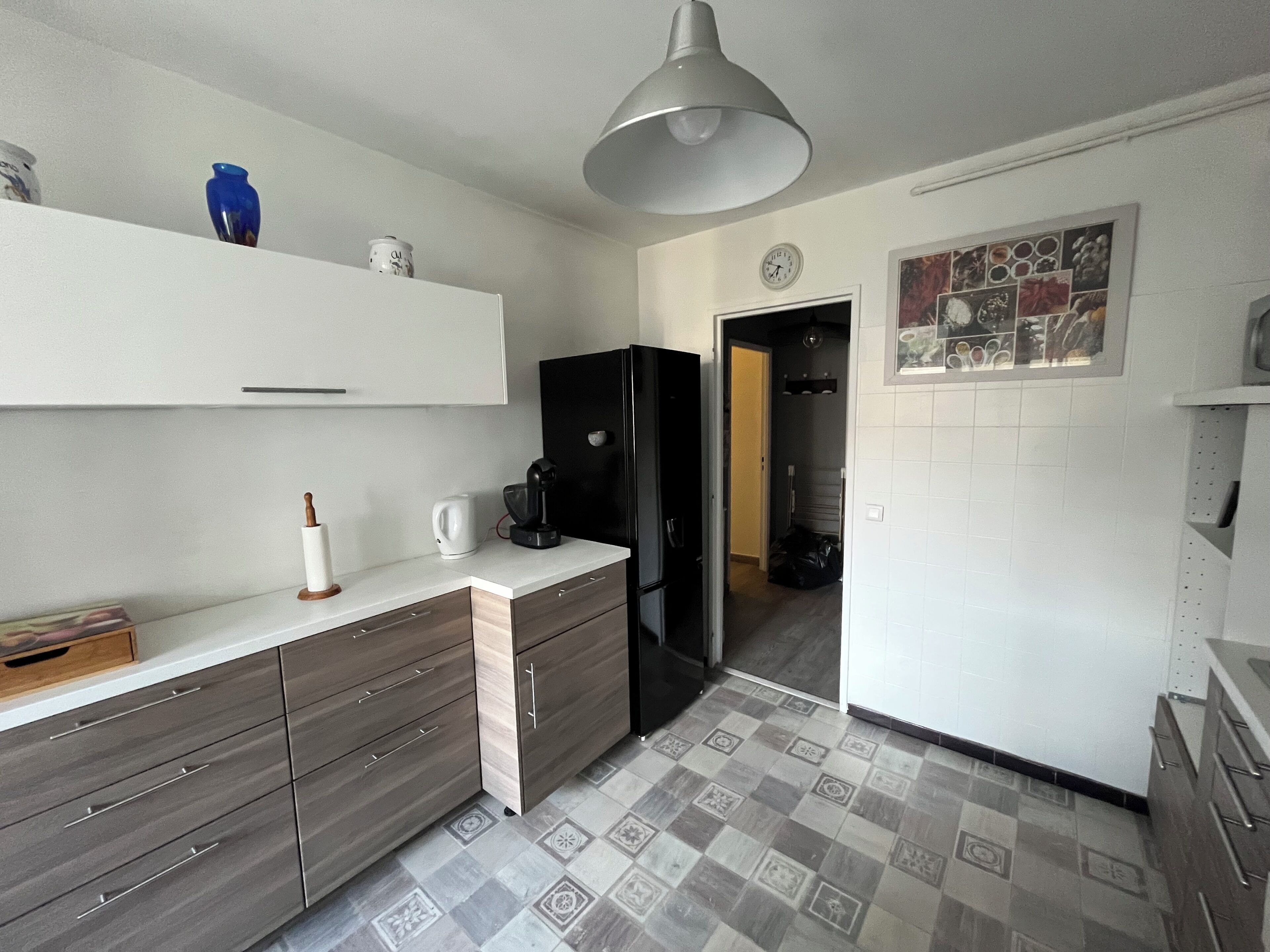 Eine Küche mit einem schwarzen Kühlschrank, einer Kaffeemaschine und einem weißen Schrank.