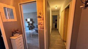 Un pasillo con un aparador, un espejo y una planta. Hay una puerta que da a otra habitación.