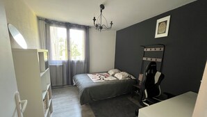 Un dormitorio con cama, una silla, un escritorio, un radiador y una ventana con cortinas.