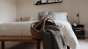 A neatly made bed with a white comforter and pillows, a bedside table with a clock, and a wall with framed pictures.