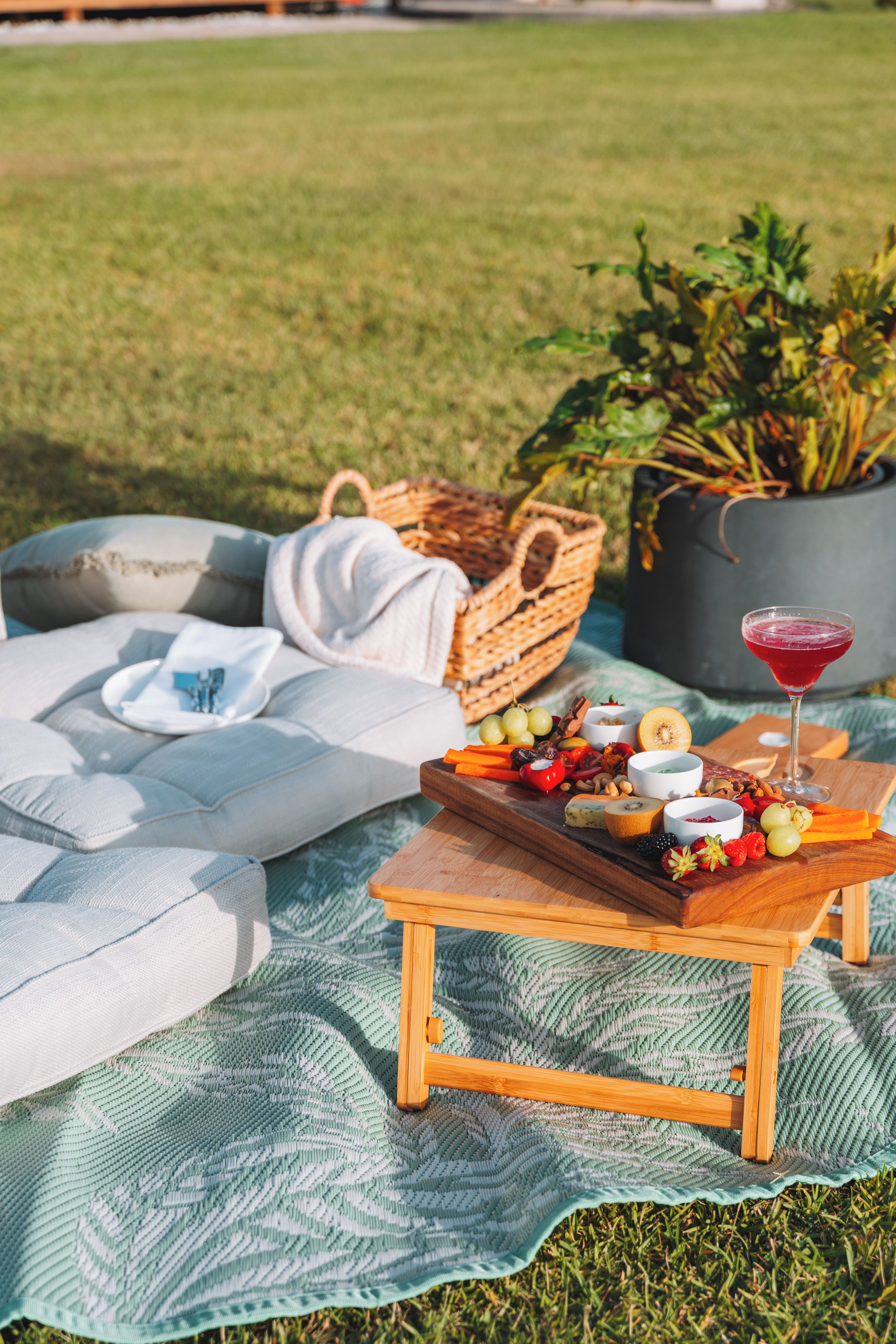 A picnic setup with a wooden tray of food and a drink on a blanket.