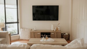 A living room with a sofa, a coffee table, a TV mounted on the wall, a wooden cabinet, and a window.