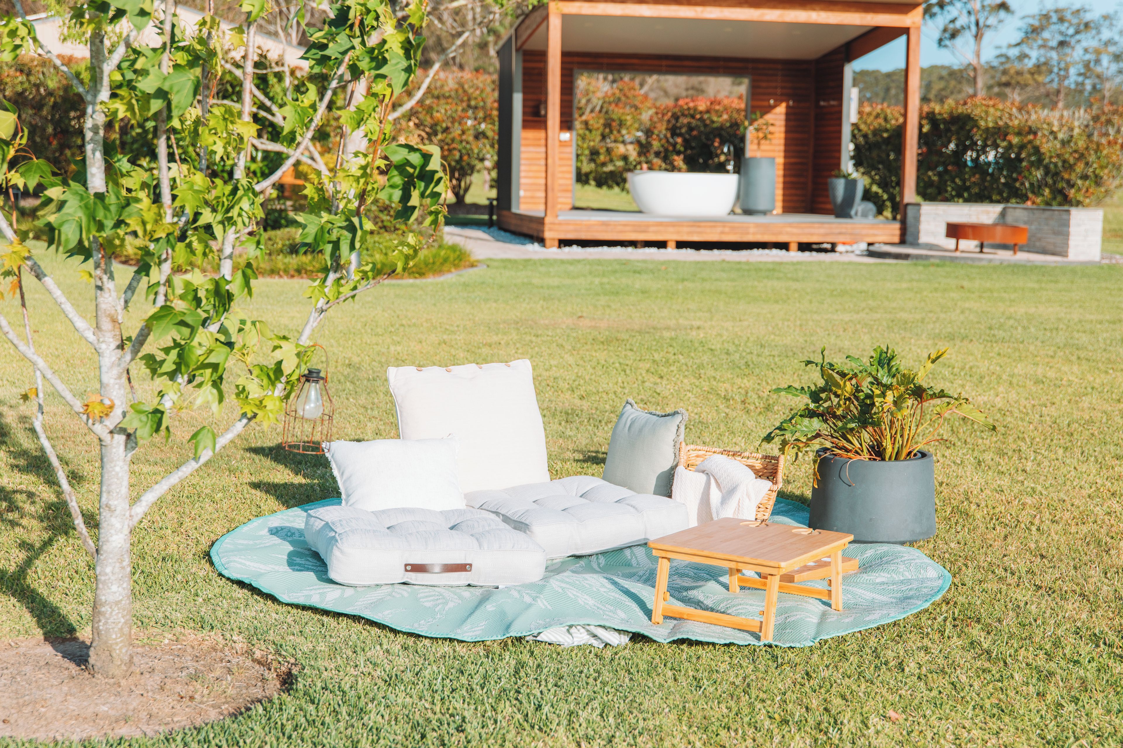 A grassy outdoor area with a modern outdoor seating arrangement including a sofa, pillows, and a small table.
