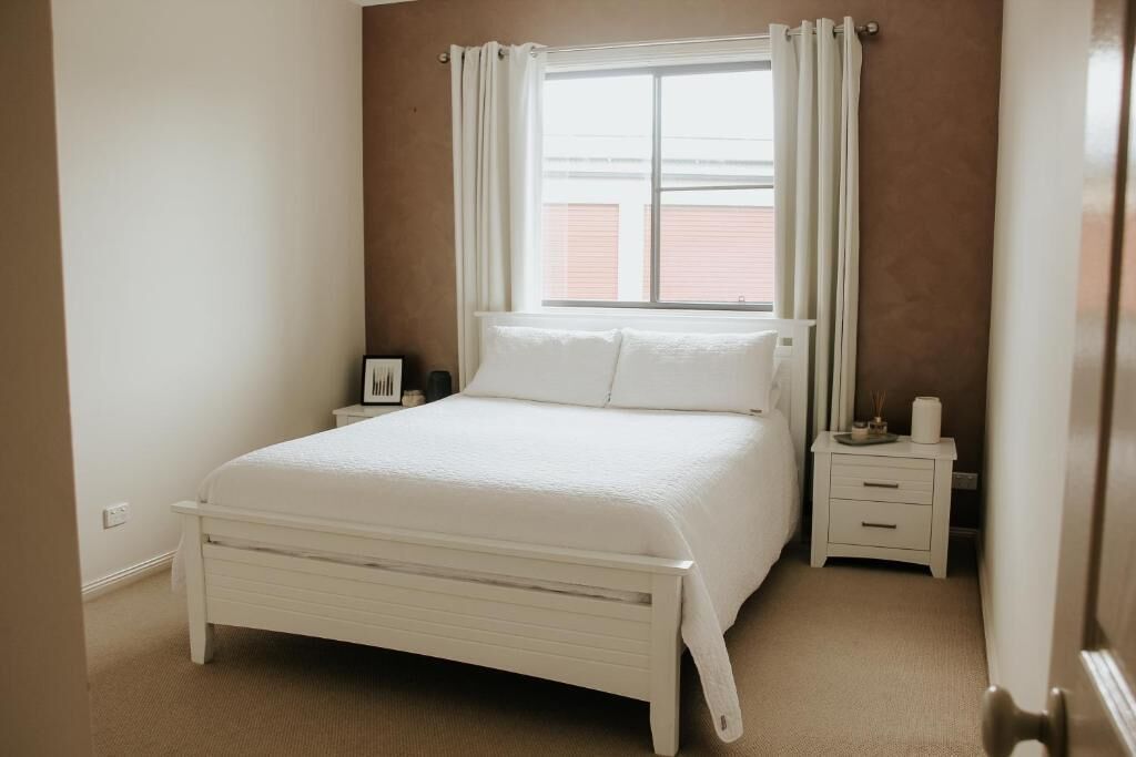 A bedroom with a bed, a nightstand, a window with curtains, and a door.
