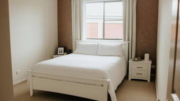 Un dormitorio con cama, mesita de noche, ventana con cortinas y puerta.
