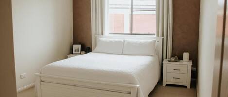 A bedroom with a bed, a nightstand, a window with curtains, and a door.