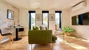 Una sala de estar moderna con un sofá verde, una mesa de comedor con sillas, una planta en maceta y cuadros en las paredes.