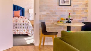 Una habitación con una cama, una mesa redonda con sillas, una pared de ladrillo y un cuadro enmarcado en la pared.